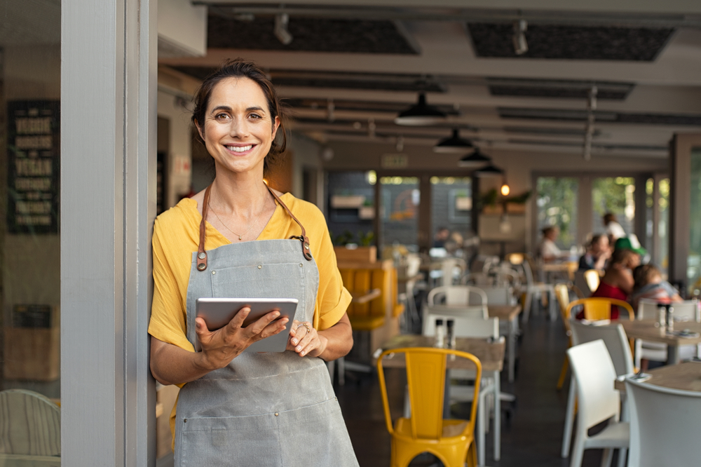 Portrait,of,happy,woman,standing,at,doorway,of,her,store.